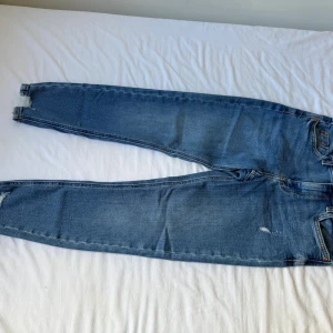 Blå skinny jeans från River Island - Säljer ett par blå skinny jeans från River Island i klassisk denim med slitna detaljer vid bensluten. Jeansen har fem fickor, normalhög midja och är tillverkade i stretchig bomullsdenim för en bekväm passform.