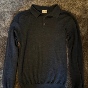 Mörkblå pikétröja i ull från John Henric - Snygg mörkblå långärmad pikétröja från John Henric. Tröjan har klassisk krage, knäppning med tre knappar och är tillverkad i merino ull. Perfekt för dig som gillar stilrena och bekväma plagg med en tidlös look.