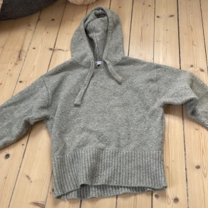 Grå stickad hoodie från Zara - Mysig grå hoodie från Zara i stickat material. Tröjan har huva med snörning och bred ribbad mudd nedtill. Perfekt för kyliga dagar och enkel att matcha med jeans eller leggings.