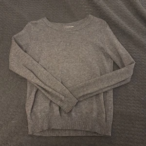 Grå stickad tröja från VILA XS - Mysig grå stickad tröja från VILA i storlek XS. Tröjan har rund halsringning, långa ärmar och breda ribbade muddar vid ärmslut och nederkant. Perfekt för lager-på-lager och chill dagar.