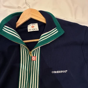 Casablanca knitted tennis sweatshirt - Snygg stickad marinblå tenniskofta från Casablanca med gröna och vita ränder längs dragkedjan och kragen. Tröjan har lång ärm, hel dragkedja framtill och broderad logga på bröstet. Perfekt för dig som gillar stilren design med sportig touch.