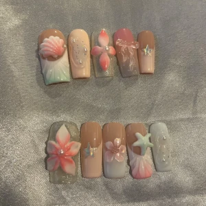 S - Press-on naglar med 3D-blommor & snäckskal - Superfina press-on naglar i nude, rosa och pastellblå toner med 3D-blommor, snäckskal, stjärnor och pärldekor. Mix av glansiga och skimrande ytor, vissa med glitter och transparent bas. Perfekt för dig som vill ha unika och detaljerade naglar med somrig vibe.