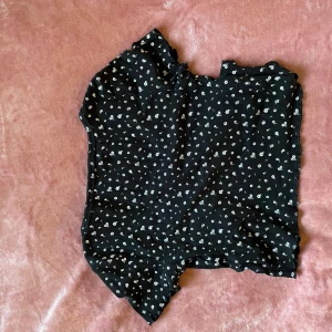 Svart blommig blus med knappar - Supersöt svart blus från Newyorker med små vita blommor över hela tyget. Blusen har korta ärmar, knappar längs ryggen och en lätt croppad passform. Perfekt för dig som gillar romantiska och trendiga plagg med fina detaljer!! (Oops ber om ursäkt för de dåliga bilderna de hamnade lite snett 😅)