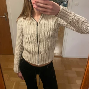 Beige stickad kofta   - Säljer en beige/kittfärgad zipkofta från PeakPerfomance med grovstickat och virkat material med fina detaljer. Koftan har en hög ribbad krage som går att fälla ner, långa ärmar och breda muddar. Har även fina, diskreta fickor på sidorna.