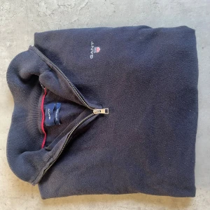 half zip tröja från GANT - Svart långärmad tröja från GANT med half zip och liten broderad logga på bröstet. Tillverkad i en skön blandning av bomull och ull. Perfekt för lager-på-lager och snygg till jeans.