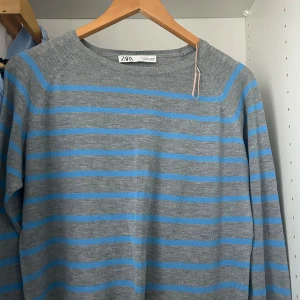 Gråblå randig stickad tröja Zara - Grå stickad tröja från Zara med blå horisontella ränder. Modellen är croppad med rund halsringning och långa ärmar. Perfekt för dig som gillar en chill och stilren look. Skön och lätt att matcha till jeans eller kjol.