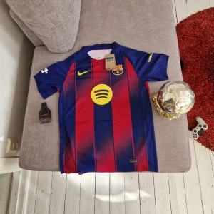 FC Barcelona Lamine Yamal 10 Nike tröja M Helt ny med Tags - Säljer en officiell FC Barcelona matchtröja från Nike med Lamine Yamal och nummer 10 på ryggen. Tröjan är blå och röd med gula detaljer, randigt mönster och klubbmärke på bröstet. Tillverkad i Dri-FIT material för bästa komfort. Champions League-märke på ärmen. Tagsen kvar, helt ny! Fick i present men den passar ej så därav säljer jag.