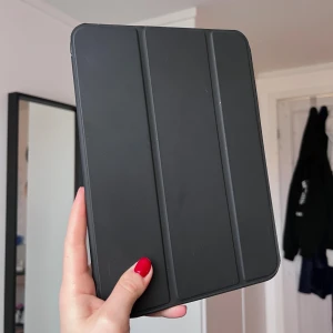 Svart iPad-skal med stativfunktion - Säljer ett stilrent svart iPad-fodral med smart stativfunktion. Fodralet har magnetisk framsida som kan vikas för att ställa upp iPaden, perfekt för att kolla på serier eller plugga. Passar till iPad generation 10 ❤️