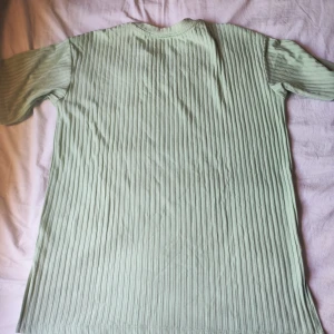 Ribbad ljusgrön t-shirt från H&M - Säljer en ribbad t-shirt i ljusgrönt från H&M. Tröjan har korta ärmar, rund halsringning och är tillverkad i mjuk bomull. Perfekt för vår och sommar när du vill ha en chill och stilren look.