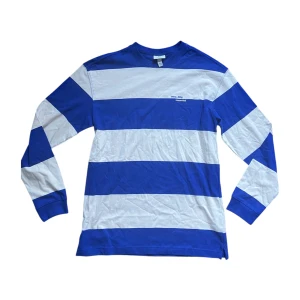 Randig blåvit långärmad tröja - Säljer en långärmad tröja från H&M med breda blå och vita ränder. Tröjan har rund halsringning och är tillverkad i mjuk bomull. Perfekt för dig som gillar en sportig och avslappnad stil.