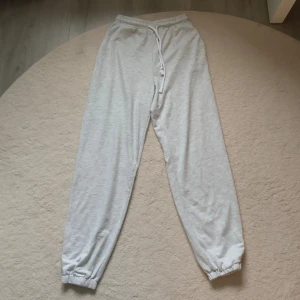 Grå mjukisbyxor med strassdetalj - Ljusgrå mjukisbyxor med resår och snörning i midjan samt resår vid bensluten. På baksidan står det 'angel' i glittriga strasstenar. Perfekta för en chill och avslappnad stil.