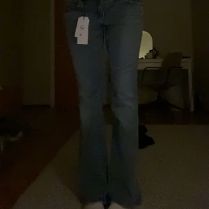 Y2K blå bootcut jeans från Gina Tricot - Säljer ett par Y2K-inspirerade blå bootcut jeans från Gina Tricot i storlek 44. Jeansen har låg midja, klassiska fickor med lock och knapp bak samt snygg tvättad denimlook. Perfekta för dig som gillar retro vibe och vill sticka ut.