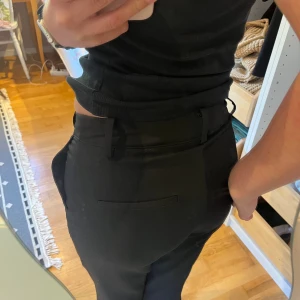 Svarta kostymbyxor från BikBok - Svarta kostymbyxor från BikBok i klassisk rak modell med diskreta bakfickor och hällor för bälte. Byxorna har en snygg midwaist/lowwaist-passform och är tillverkade i ett slätt, mjukt material som ger en clean look. Perfekta för en stilren outfit. Som du ser på sista bilden så finns det en tråd som står ut lite. Inget som syns så mycket när du har på dig dem, men bra att vara medveten om det❤️