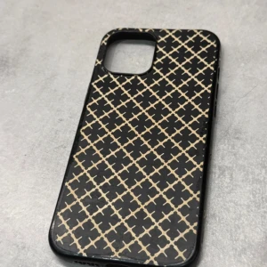 By Malene Birger iPhone Case - Stilrent iPhone-skal från By Malene Birger med svart och beige mönster. Passar modeller med större kameramodul. Skalet visar tecken på slitage runt kanterna men är i fullt fungerande skick och skyddar din mobil effektivt. iPhone 12 Pro Max 