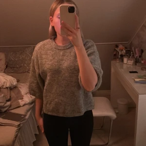 Grå stickad tröja från Gina Tricot - Mysig grå stickad tröja från Gina Tricot med rund halsringning och lite kortare, loose passform. Tröjan har långa ärmar och är perfekt för kyliga dagar. Enkel och stilren design som passar till det mesta.