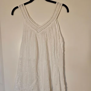 Vit sommartopp från Grekland - Supersöt vit linnetopp med breda virkade axelband och v-ringning. Köpt i Grekland. Toppen har en luftig, flowy passform. Onesize men skulle säga den passar bra för storlek S, men skulle även passa M.