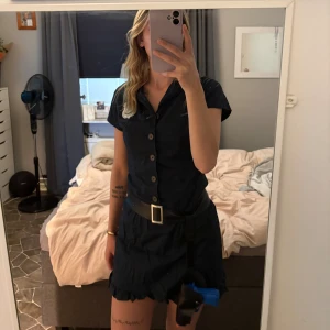 Polisklänning - Säljer en mörkblå kort polisklänning med knappar framtill, korta ärmar och tillhörande bälte med silverfärgat spänne. Klänningen har ett broderat 'Special Police'-märke på bröstet och kommer med matchande poliskeps. Perfekt för temafest eller maskerad!