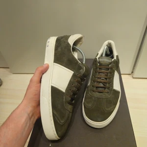 Valentino Garavani sneakers mocka - Snygga sneakers från Valentino Garavani i olivgrön mocka med vita detaljer och bruna skosnören. Klassisk låg modell med rund tå. Är lite lim på undersidan av ena skon samt lite färg på nitarna.