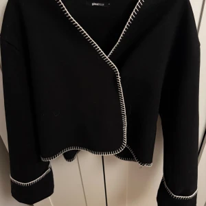 Svart kofta från Gina Tricot - Svart kofta från Gina Tricot med vit söm längst kanterna. Storlek S, aldrig använt men köpte den begagnad. Skriv för fler frågor, bilder eller prisförslag.