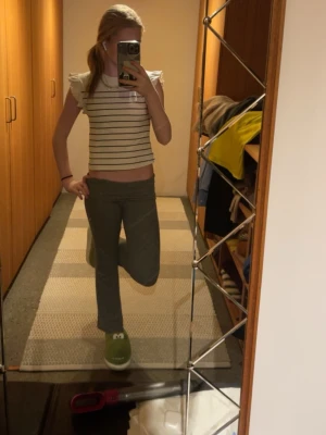 Randig croppad topp med volangärm - Säljer en vit croppad topp med svarta horisontella ränder och volangdetaljer på axlarna. Toppen är ärmlös och har en fräsch, ungdomlig stil som passar perfekt till jeans eller kjol.