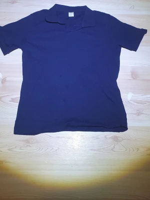 Mörkblå ribbad tshirt från Lindex - Säljer en mörkblå ribbad topp från Lindex i storlek 170. Toppen har korta ärmar, klassisk krage och är tillverkad i mjuk bomull. Perfekt för dig som gillar enkel och stilren design med lite struktur i tyget. Passar superbra till de gråa jeansen jag säljer.