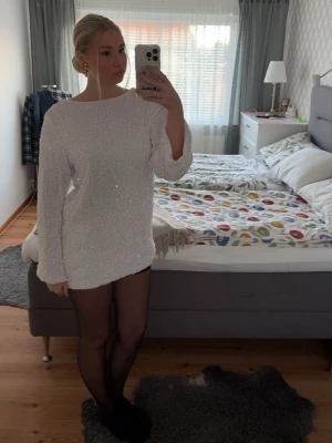 Vit glittrig kortklänning - Säljer en vit glittrig kortklänning med långärmade ärmar. Klänningen har en rak och loose passform och är täckt av små paljetter som ger ett snyggt skimmer. Perfekt för dig som vill sticka ut med en enkel men glamorös look.