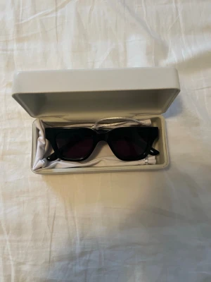 Svart solglasögon från CHIMI - Snygg svart dunväst från CHIMI med stilren design och raka linjer. Västen har en klassisk passform och är tillverkad i syntetmaterial. Perfekt för att addera en cool touch till din outfit. Västen har inga synliga mönster eller detaljer och passar dig som gillar minimalistisk stil.