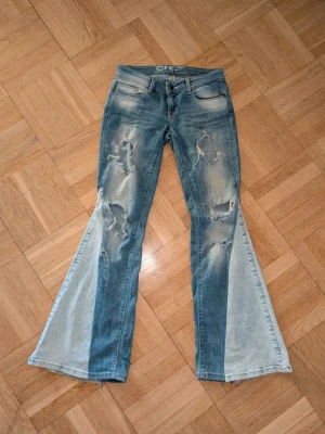 Blå bootcut jeans med slitningar - Säljer ett par blå bootcut vintage only jeans utsydda till bootcut och har hål på låren. Jeansen har låg midja och är tillverkade i denim med kontrasterande ljusare paneler nedtill. Riktigt snygga och unika jeans för dig som gillar en edgy stil.