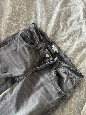 Grå jeans  - Som är ljusare i verkligheten, tror det beror på ljuset bara. Säljer ett par grå jeans från Gina Tricot med klassisk femficksdesign och raka ben. Jeansen har normal midja, dragkedja och knapp framtill samt snygga slitningar för en cool look. Perfekta för dig som gillar enkel och stilren denim.