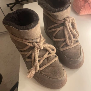 Beige boots från Inuikii - Säljer ett par snygga beigea boots från Inuikii med grova snören och mjukt foder. Skorna är i mocka och skinn, perfekta för kalla dagar. De har en platt sula och rund tå, samt broderad logga bak. 
