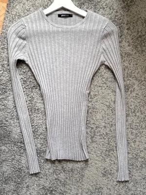 Grå ribbad långärmad topp  - Säljer en ljusgrå långärmad topp med ribbad struktur. Modellen är slim fit och har rund halsringning. Perfekt att styla med jeans eller kjol för en clean look.