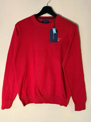 Röd GANT tröja i bomull, S - Skick: 10/10!! Nypris 1400kr. Säljer för 800. Storlek S, men du får plats med en skjorta under! Tröjan har rund hals, ribbade muddar och ett broderat GANT-logo på bröstet. Tillverkad i mjuk bomull, perfekt för dig som gillar klassisk stil med en modern touch. Perfekt nu till jul!