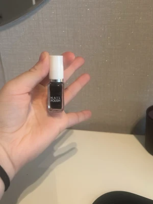 Svart nagellack med vit kork - Snyggt svart nagellack i en liten fyrkantig glasflaska med vit plastkork och silverdetalj. Perfekt för att skapa en cool och edgy look på naglarna. Lätt att applicera med den medföljande penseln.