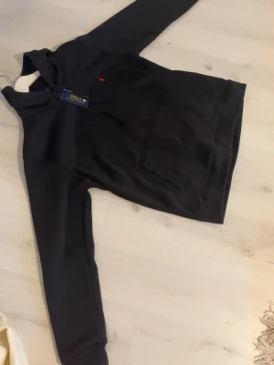 Ralph Lauren - Svart hoodie med röd Ralph Lauren-logotyp på bröstet. Klassisk och stilren design i mjukt och bekvämt material. Fick som present har inte kommit till någon användning. Hör av dig vid frågor elller funderingar.