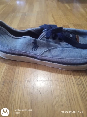 Blå sneakers från Polo Ralph Lauren - Säljer ett par blå sneakers från Polo Ralph Lauren med klassisk broderad logga på sidan. Skorna har rund tå, platt vit sula och snörning i mörkblått. Tillverkade i bomullstyg som ger en avslappnad och stilren look.