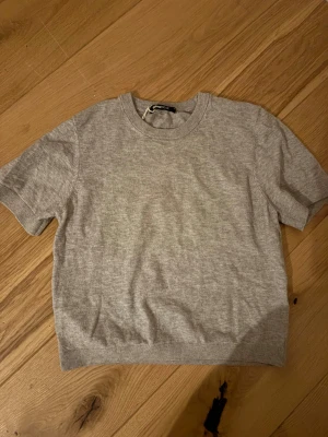 Grå kortärmad t-shirt från Gina Tricot - En enkel och stilren grå t-shirt från Gina Tricot i storlek S. T-shirten har korta ärmar, rund hals och är gjord i mjuk bomull. Passar perfekt till jeans eller shorts och har en klassisk, avslappnad look.