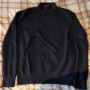 Mörkblå stickad polotröja - Säljer en mörkblå stickad polotröja från Selected Homme. Tröjan har lång ärm och en högre krage som ger en clean och stilren look. Perfekt för lager-på-lager och funkar till både jeans och kostymbyxor.