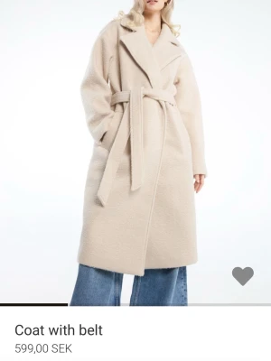 Beige kappa med bälte - Säljer en snygg beige kappa med breda slag och knytbälte i midjan. Jackan har en mjuk och fluffig yta som ger en chill vibe och är perfekt för kyliga dagar. Lång modell med fickor på sidorna och avslappnad passform.