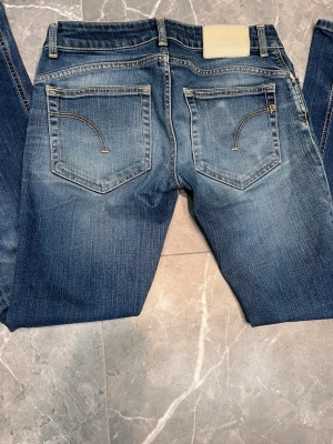 Blå Dondup jeans - Säljer ett par snygga blå jeans från Dondup, modell Lambda med tvätt Broadpeak. Jeansen har klassisk femficksdesign, kontrastsömmar och en cool faded effekt. Materialet är 94% bomull och 6% polyester, vilket gör dem både bekväma och slitstarka.