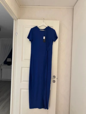 Blå långklänning från Vero Moda - Snygg blå långklänning från Vero Moda med rund halsringning och korta ärmar. Klänningen har en slits. 