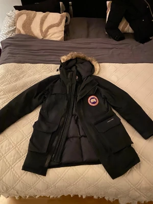 Svart dunjacka från Canada Goose - Jag säljer en riktigt snygg Svart dunjacka från Canada Goose med pälskantad huva och klassisk logga på bröstet. Jackan har flera stora fickor, dragkedja och quiltad insida. Perfekt för kalla vinterdagar och har en riktigt snygg streetstil. 9/10 skick✅.  Storlek S/Small men passar på M/Medium 