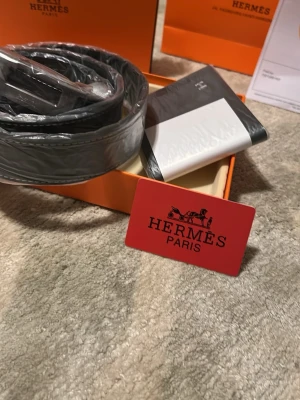 Svart skinnväst från Her-més med H logga  - Exklusiv svart väst från Her - més  i äkta skinn med stilren design och diskreta sömmar. Västen har klassisk form och levereras med originalförpackning och äkthetskort. Perfekt för dig som vill ha en lyxig och tidlös look. Allt på bilden kommer med och priset kan diskuteras ( helt ny ) 110cm