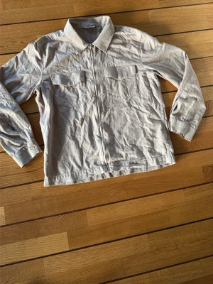 Beige overshirt från Weekday - Säljer en beige overshirt från Weekday med dragkedja framtill och två bröstfickor. Jackan har klassisk krage och är långärmad, perfekt för lager-på-lager. Materialet är bomull och passformen är normal.