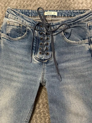 Blå bootcut jeans med snörning Pull&Bear - Säljer ett par ljusblå bootcut jeans från Pull&Bear i storlek 38. Jeansen har snygg snörning framtill, klassiska fem fickor och råa kanter längst ner. Tillverkade i jeansmaterial med en cool tvättad look.