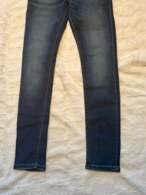 Tommy Hilfiger blå skinny jeans 152 - Snygga blå jeans från Tommy Hilfiger i skinny fit med klassiska fem fickor och tydliga kontrastsömmar. Jeansen har en mörk tvätt med lätt slitning och är tillverkade i mjukt bomullsmaterial med stretch. Perfekt för dig som gillar en smal siluett och stilren look.