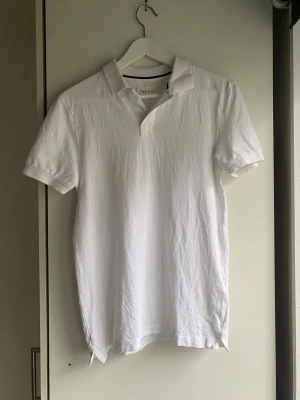 Vit piké från Pier One - Klassisk vit pikétröja från Pier One med korta ärmar och krage. Tillverkad i mjuk bomull som känns skön mot huden. Tröjan har en enkel design med två knappar vid halsen och en rak passform. Perfekt för en clean och fräsch look.