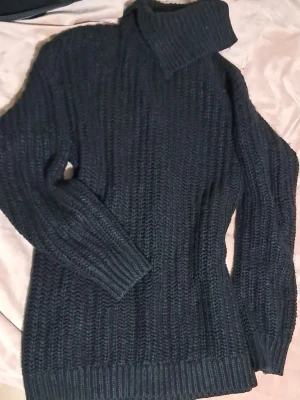 Svart stickad klänning från Lindex - Säljer en svart, grovstickad klänning från Lindex i storlek S. Tröjan har lång ärm, ribbade muddar och hög polokrage som ger extra mysfaktor. Perfekt för kyliga dagar och enkel att matcha med jeans eller kjol.