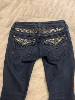 Miss Me jeans med paljettdetaljer - Snygga mörkblå jeans från Miss Me i storlek 25. Byxorna har bootcut-snitt och är dekorerade med glittriga paljetter och mönstrade detaljer på fickorna både fram och bak. Små nötta längst ner vid benen, se två sista bilder. Pris kan diskuteras.