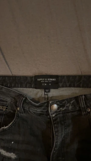 Supply & Demand svarta skinny jeans - Svarta jeans från Supply & Demand med slitna detaljer och trasiga partier på benen. Skinny fit med normal midja och klassisk femficksdesign. Jeansen har en tvättad look och dragkedja i gylfen. Perfekt för dig som gillar streetstyle.