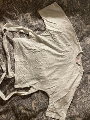 Vit med knytband - Säljer en vit fin topp med knytning på ryggen  från Nelly i mjuk bomull. Toppen har korta ärmar och långa knytband som kan snurras runt ryggen💕